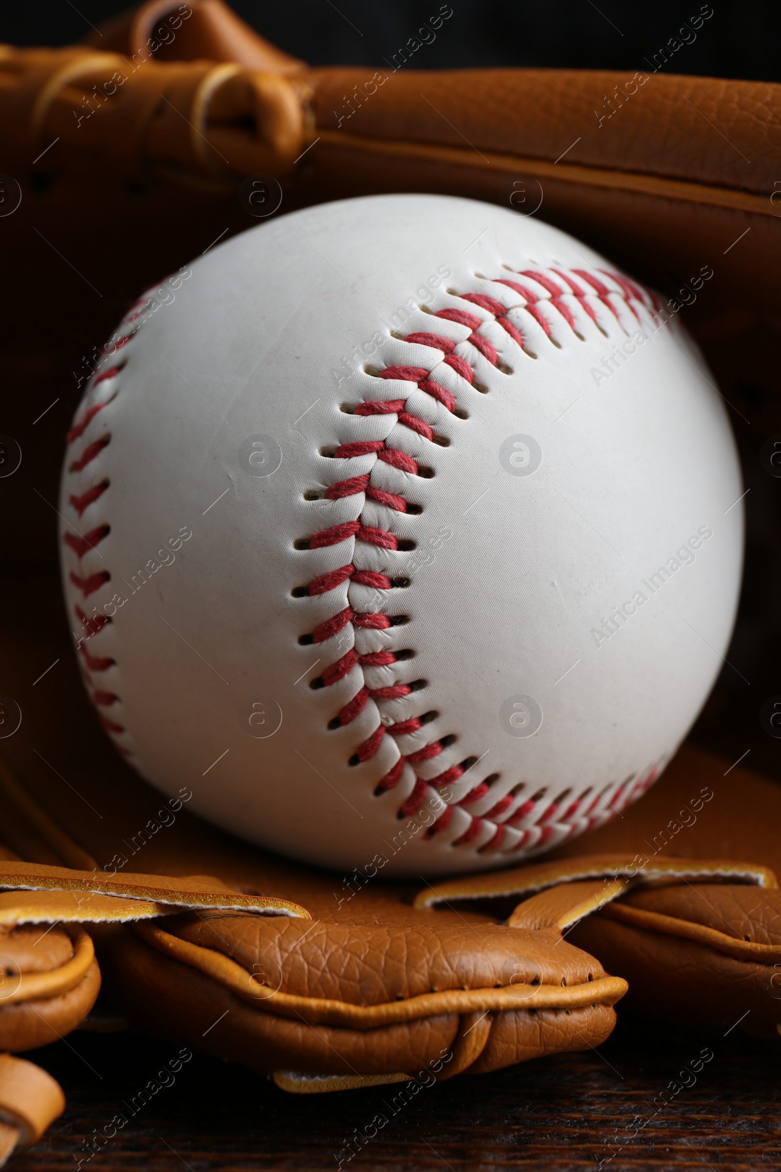 Photo of Leather baseball glove with ball on wooden table, closeup