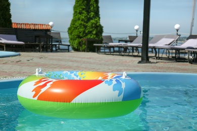 Colorful inflatable ring floating in swimming pool on sunny day, outdoors. Space for text