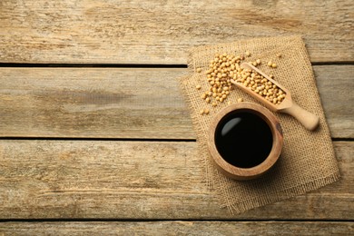 Soy sauce in bowl and soybeans on wooden table, flat lay. Space for text