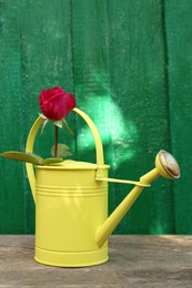 Photo of Yellow watering can with beautiful rose on wooden table