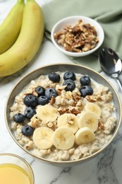 Photo of Tasty oatmeal with banana, blueberries, walnuts and milk served in bowl on white marble table