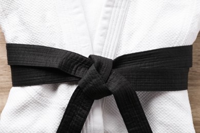 Photo of Martial arts uniform with black belt on white wooden background, closeup