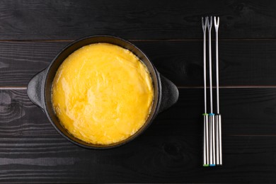 Photo of Fondue pot with melted cheese and forks on black wooden table, top view