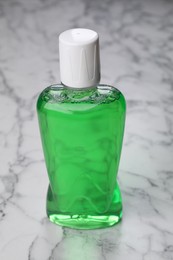 Photo of Fresh mouthwash in bottle on white marble table, closeup