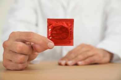 Photo of Doctor holding condom at wooden table, closeup. Safe sex concept