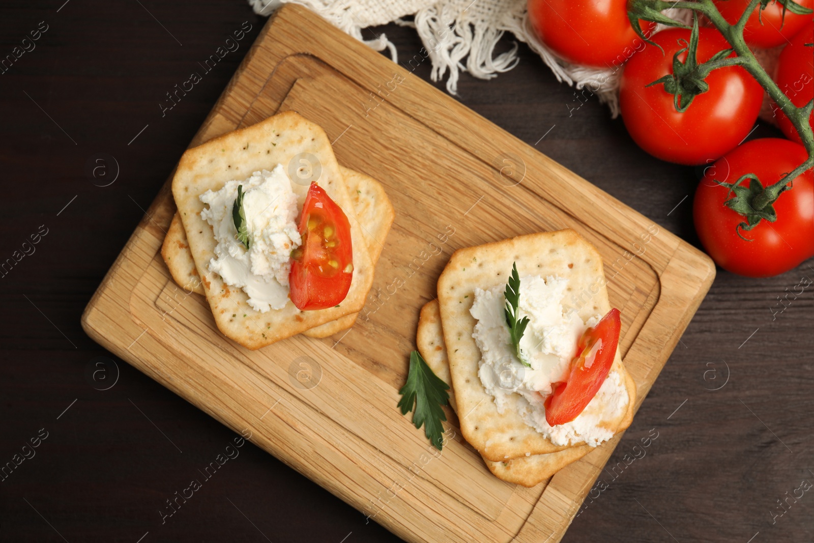 Photo of Delicious crackers with cream cheese, tomato and parsley on wooden table, flat lay