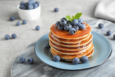 Photo of Plate of delicious pancakes with fresh blueberries and syrup on grey table