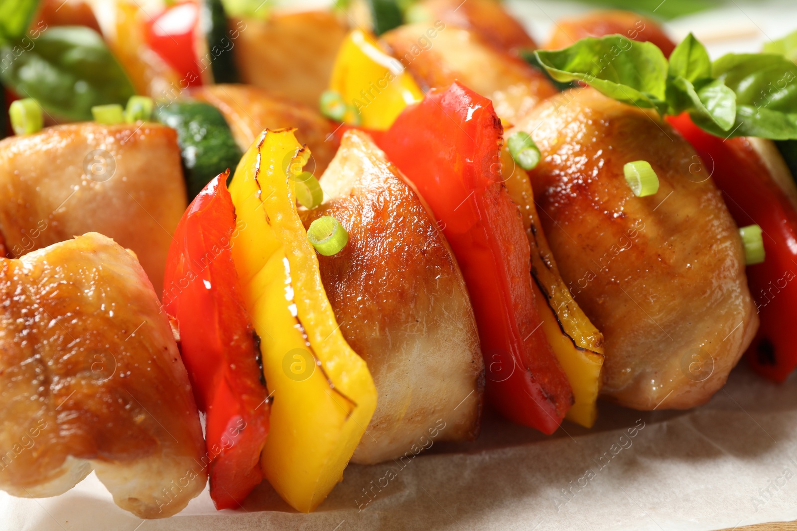 Photo of Delicious chicken shish kebabs with vegetables on parchment, closeup
