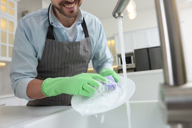 Man washing plate above sink in kitchen, closeup