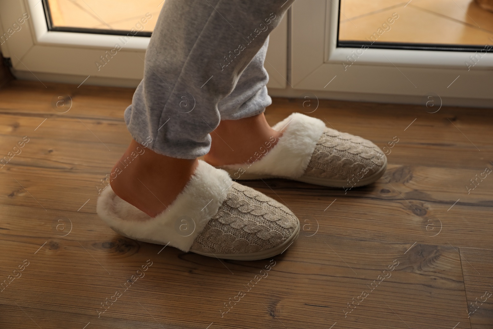 Photo of Woman wearing warm beige slippers on wooden floor, closeup