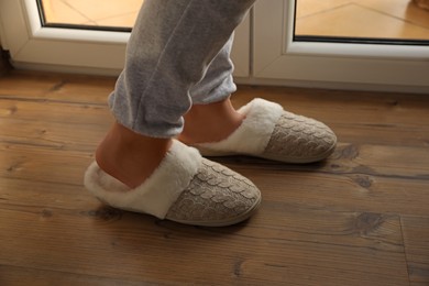 Woman wearing warm beige slippers on wooden floor, closeup