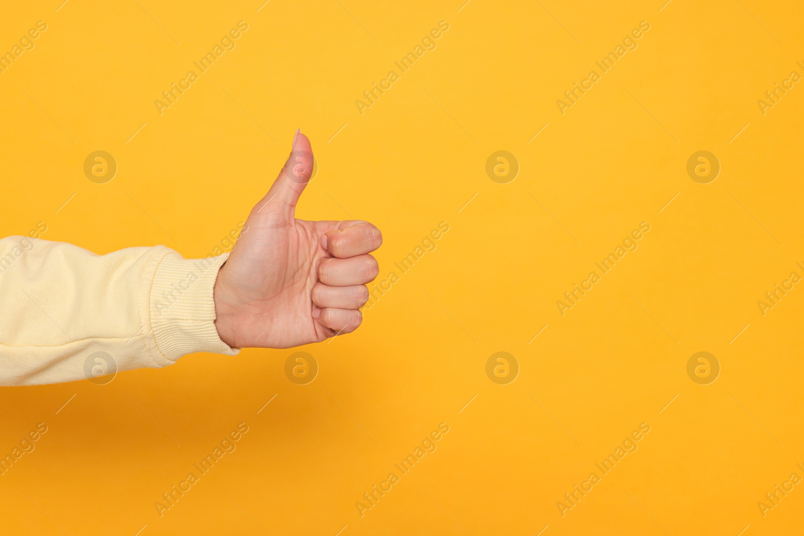 Photo of Woman showing thumb up on orange background, closeup. Space for text