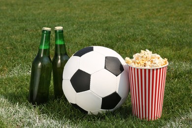 Photo of Football ball with beer and popcorn on green field grass