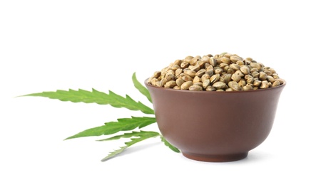 Bowl of hemp seeds with green leaf on white background