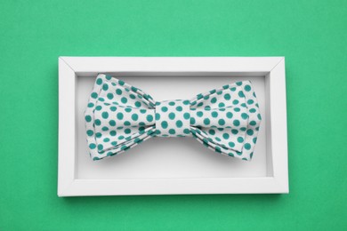 Stylish bow tie with polka dot pattern in box on green background, top view