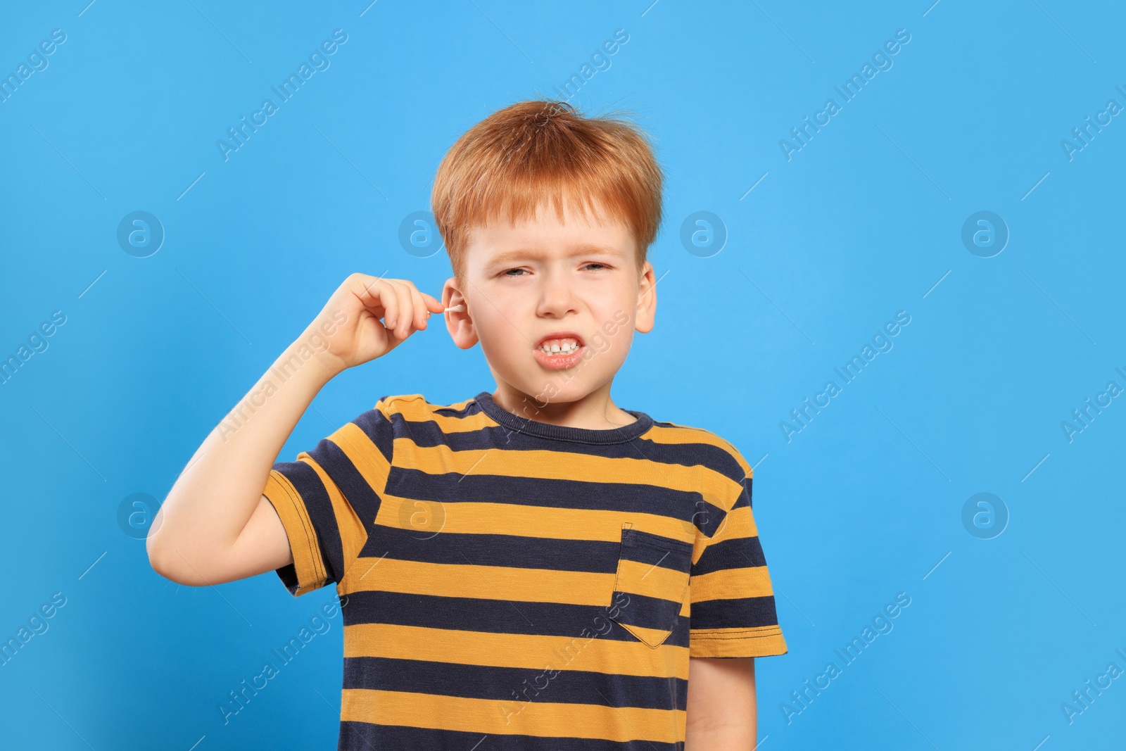 Photo of Little boy cleaning ear with cotton swab on light blue background