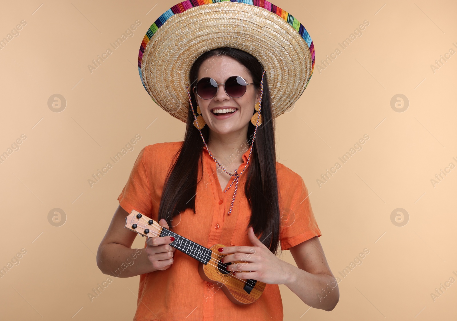 Photo of Young woman in Mexican sombrero hat playing ukulele on beige background