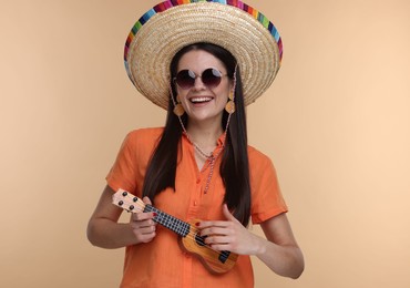 Photo of Young woman in Mexican sombrero hat playing ukulele on beige background