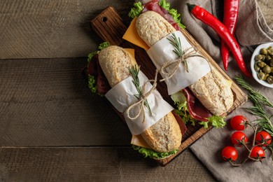 Photo of Delicious sandwiches with bresaola, lettuce and other products on wooden table, flat lay. Space for text