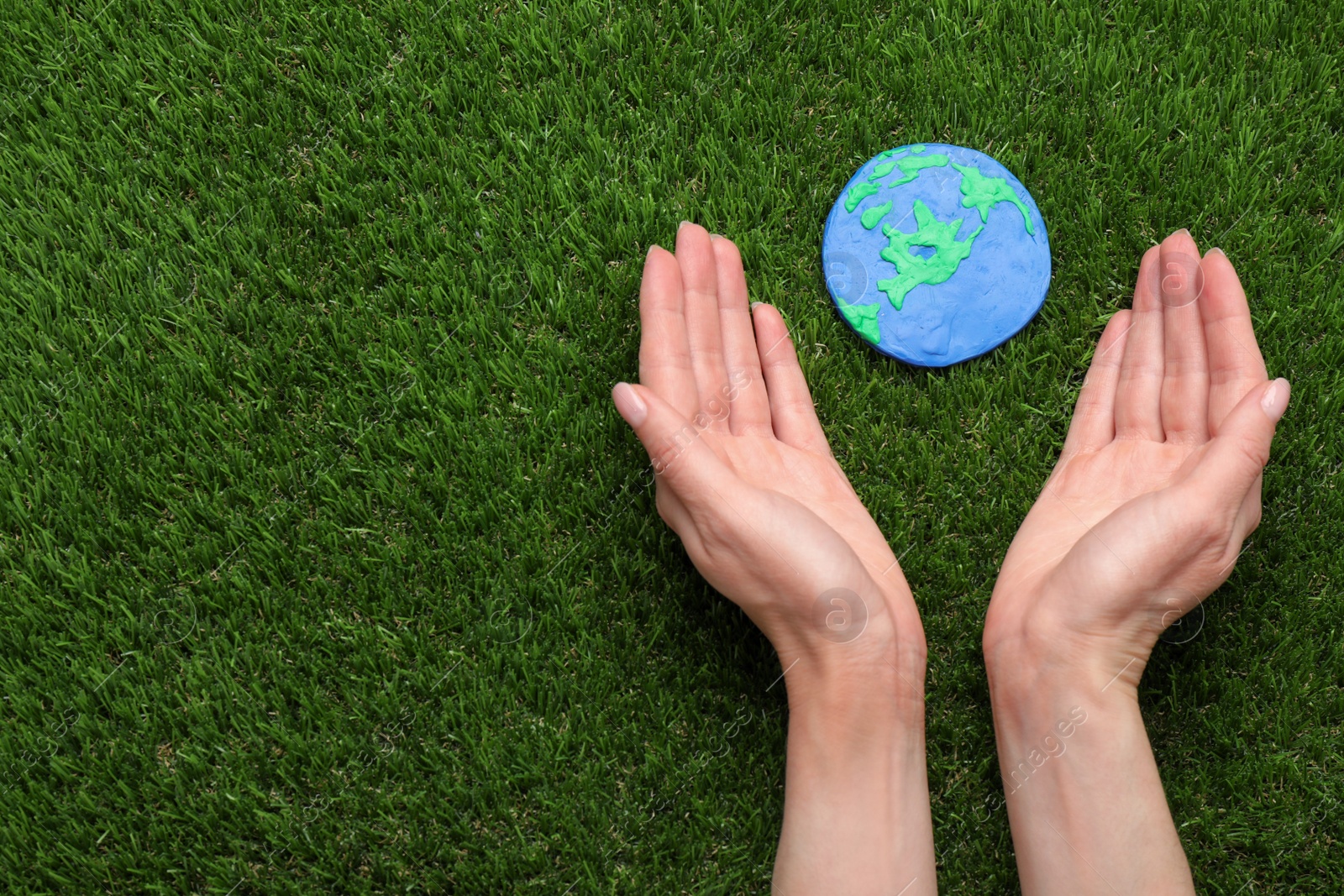 Photo of Happy Earth Day. Woman with plasticine planet on green grass, top view and space for text