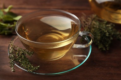 Photo of Cup of aromatic herbal tea and fresh thyme on wooden table, closeup