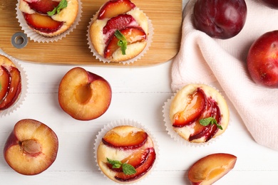 Photo of Delicious cupcakes with plums on white wooden table, flat lay