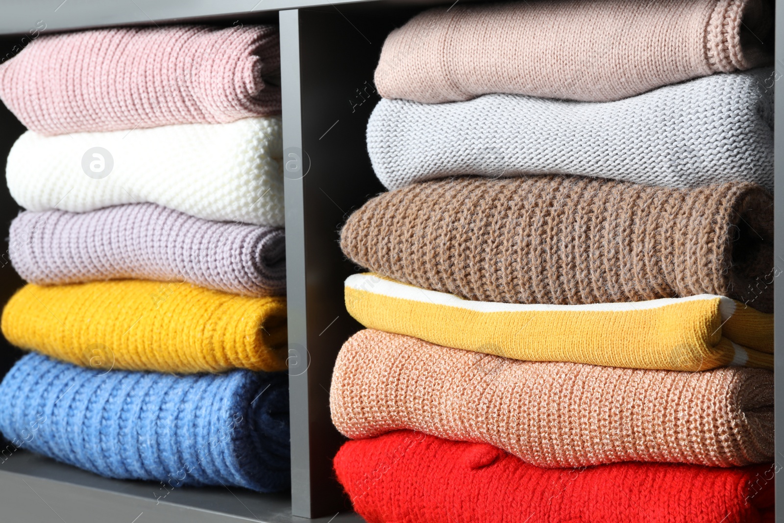 Photo of Many knitted winter clothes stacked on shelves, closeup