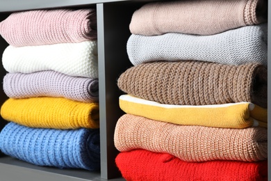 Many knitted winter clothes stacked on shelves, closeup