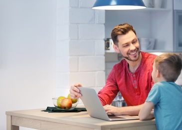 Little boy and his dad using laptop at home