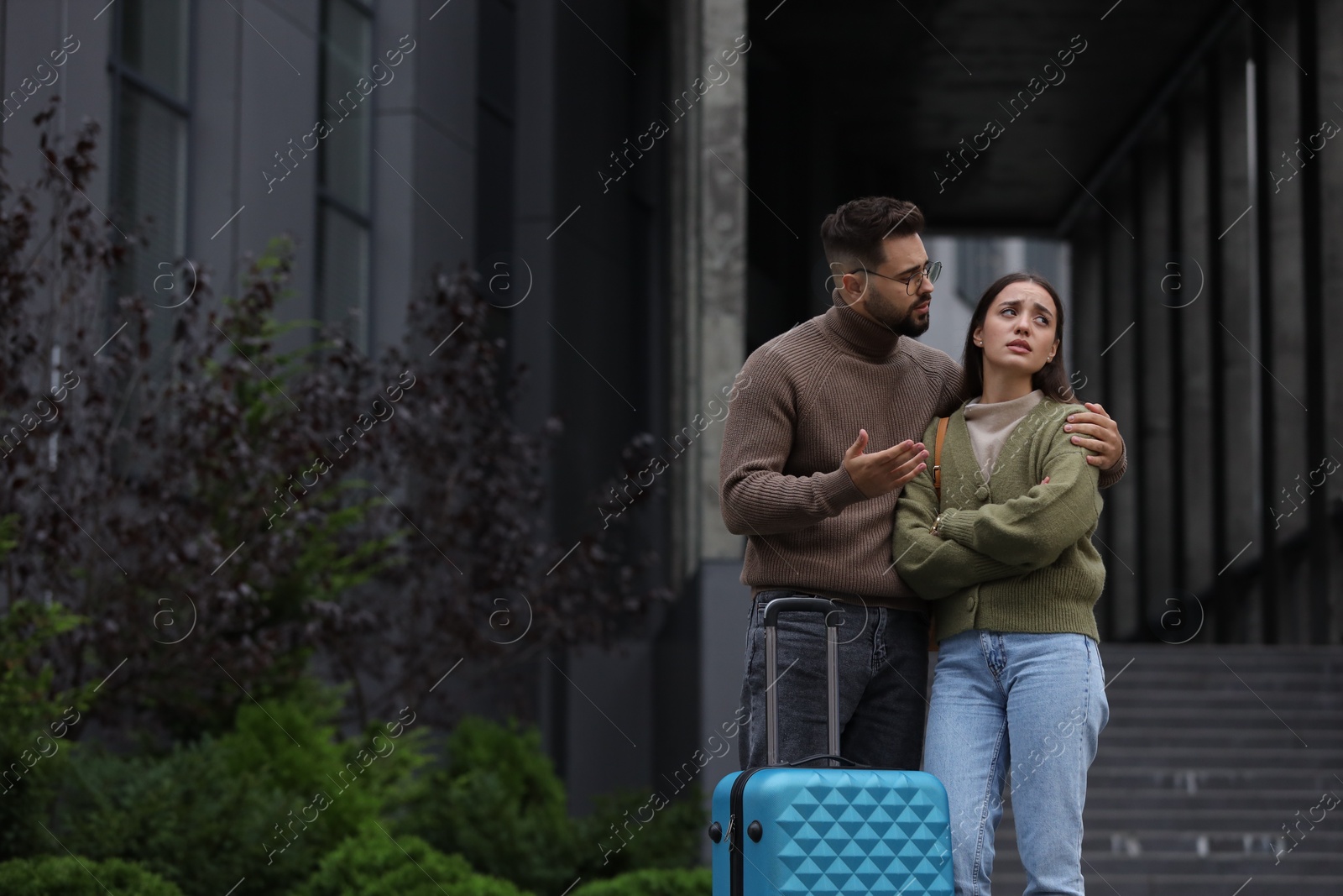 Photo of Being late. Worried couple with suitcase near building outdoors, space for text