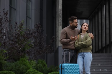 Being late. Worried couple with suitcase near building outdoors, space for text