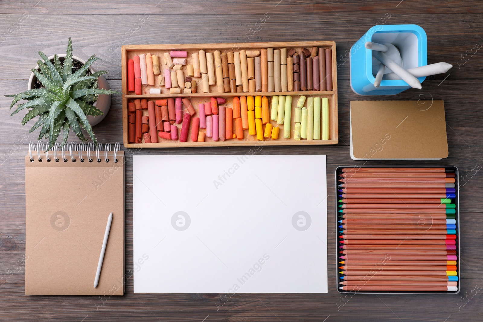 Photo of Blank sheet of paper, colorful chalk pastels and drawing pencils on wooden table, flat lay. Modern artist's workplace