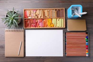 Blank sheet of paper, colorful chalk pastels and drawing pencils on wooden table, flat lay. Modern artist's workplace