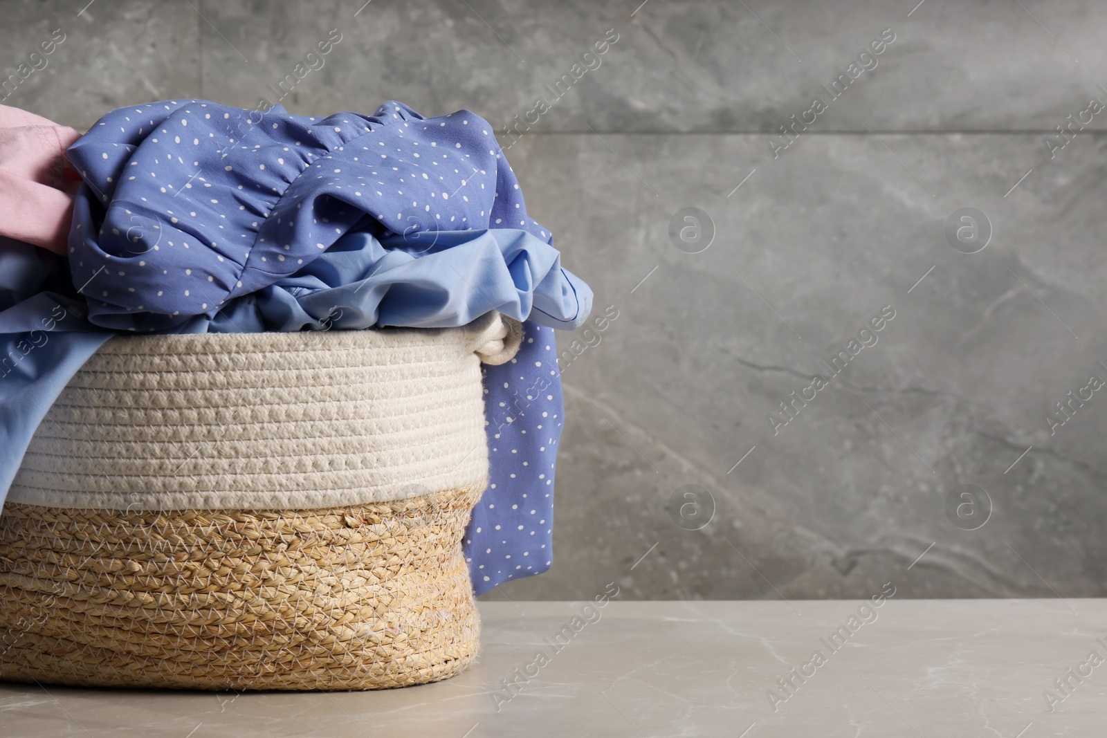 Photo of Laundry basket with clothes near grey wall. Space for text