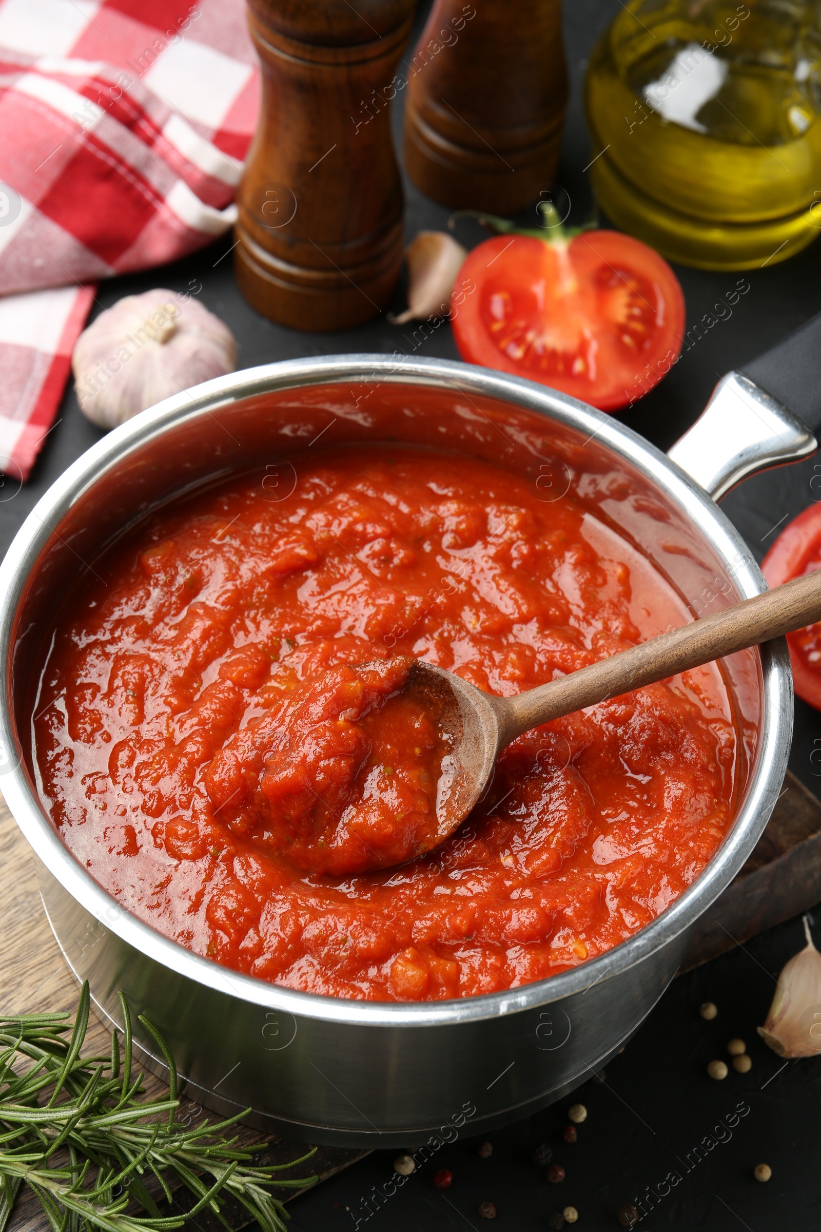 Photo of Homemade tomato sauce in pot, spoon and ingredients on dark table