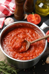 Homemade tomato sauce in pot, spoon and ingredients on dark table