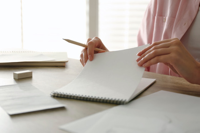 Woman with pencil and notepad at wooden table, closeup