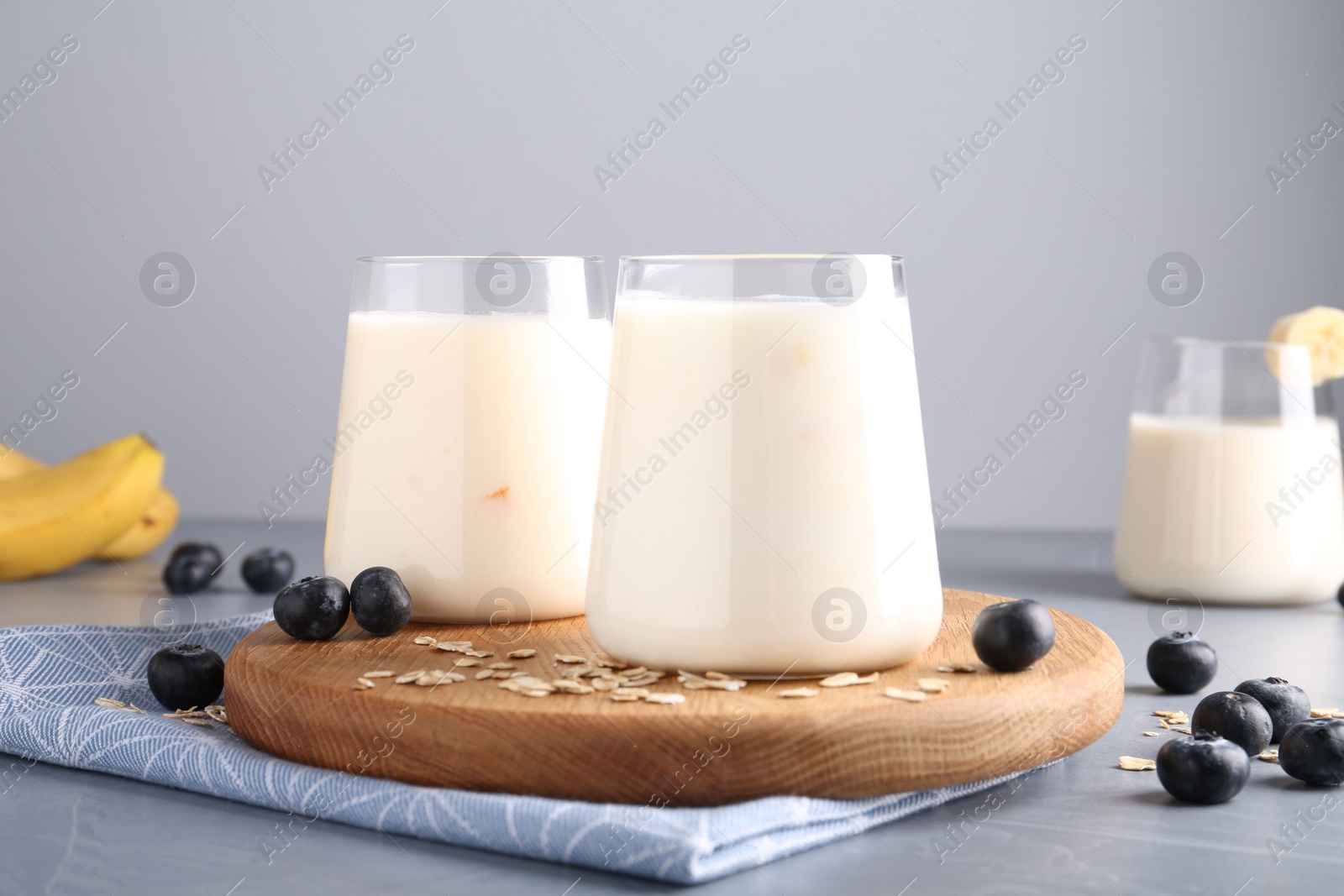 Photo of Tasty yogurt in glasses, oats and blueberries on grey table