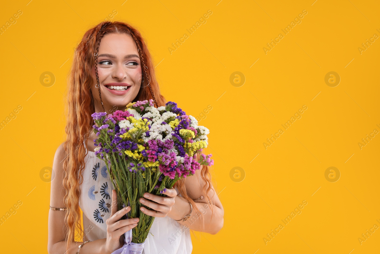 Photo of Beautiful young hippie woman with bouquet of colorful flowers on orange background, space for text