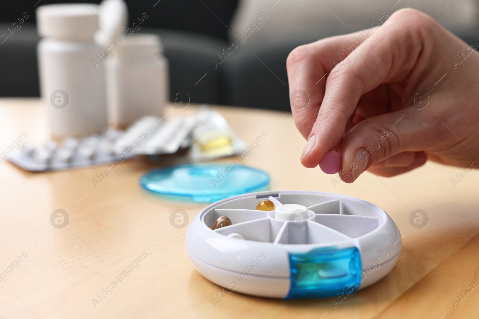 Photo of Woman with pills and organizer at light wooden table, closeup