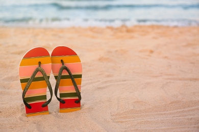 Photo of Stylish flip flops on sand near sea, space for text. Beach accessories