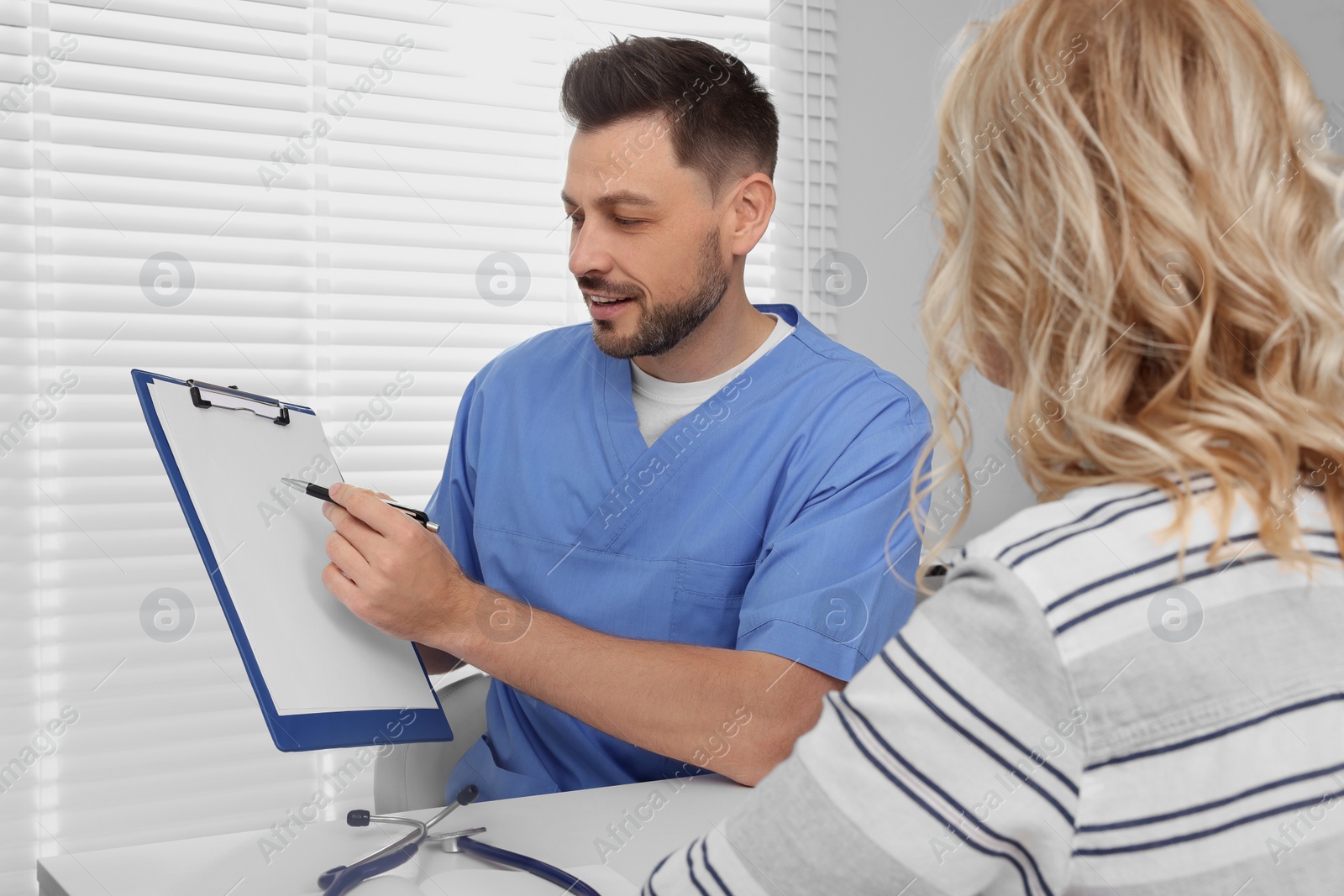 Photo of Doctor with clipboard consulting patient in clinic