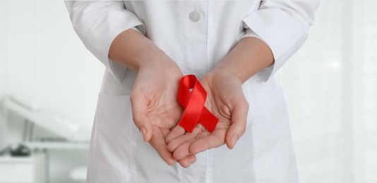 Image of Cancer awareness. Doctor holding red ribbon on blurred background, closeup. Banner design