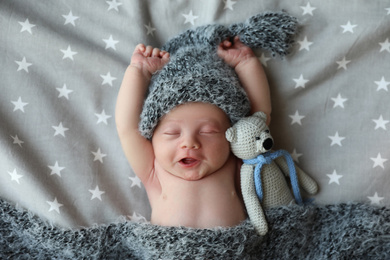 Cute newborn baby in warm hat with toy sleeping on bed, top view