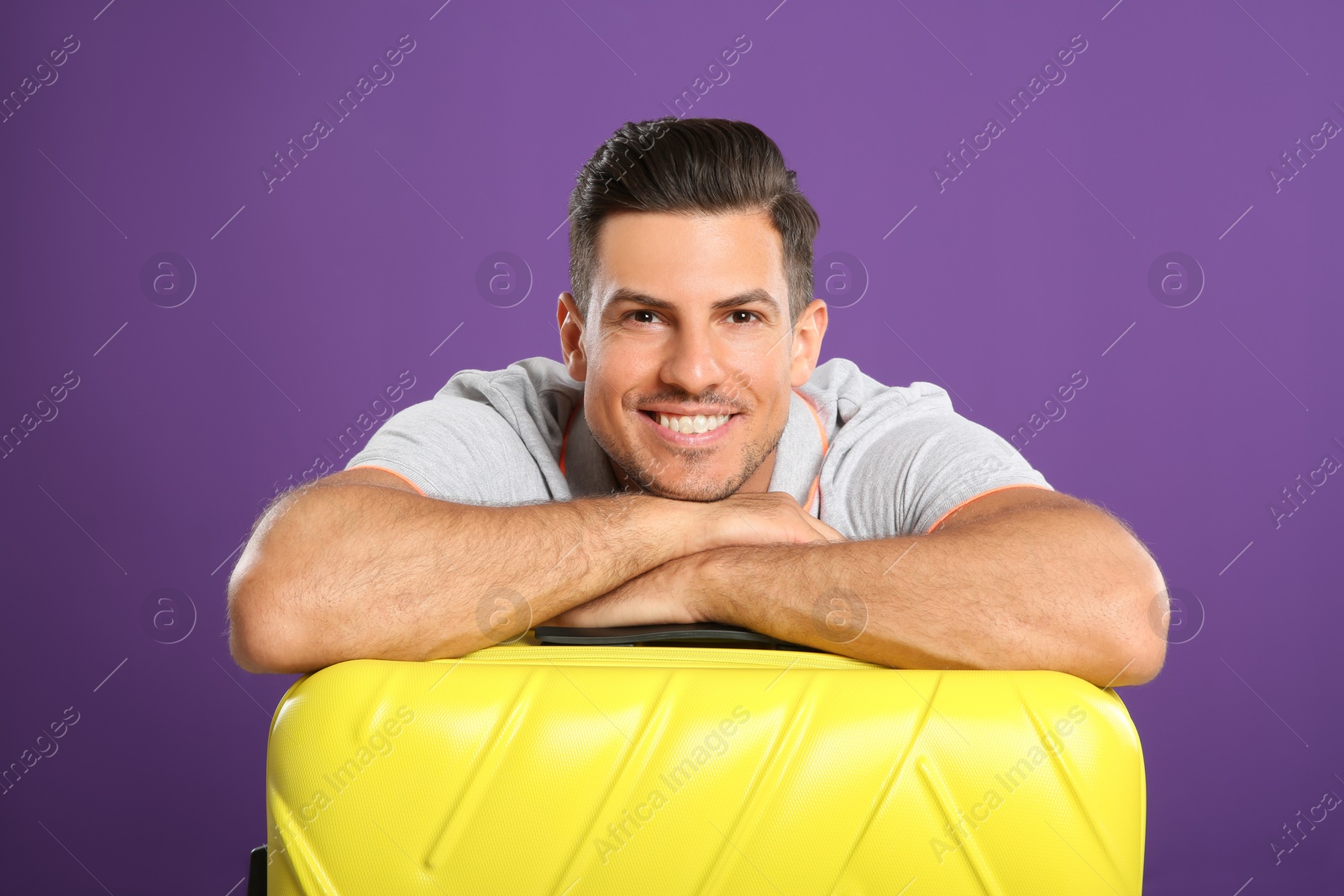 Photo of Handsome man with suitcase for summer trip on purple background. Vacation travel