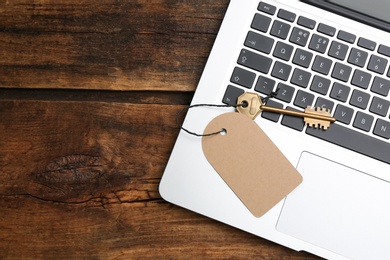 Photo of Metal key with blank tag and laptop on wooden table, top view. Keyword concept