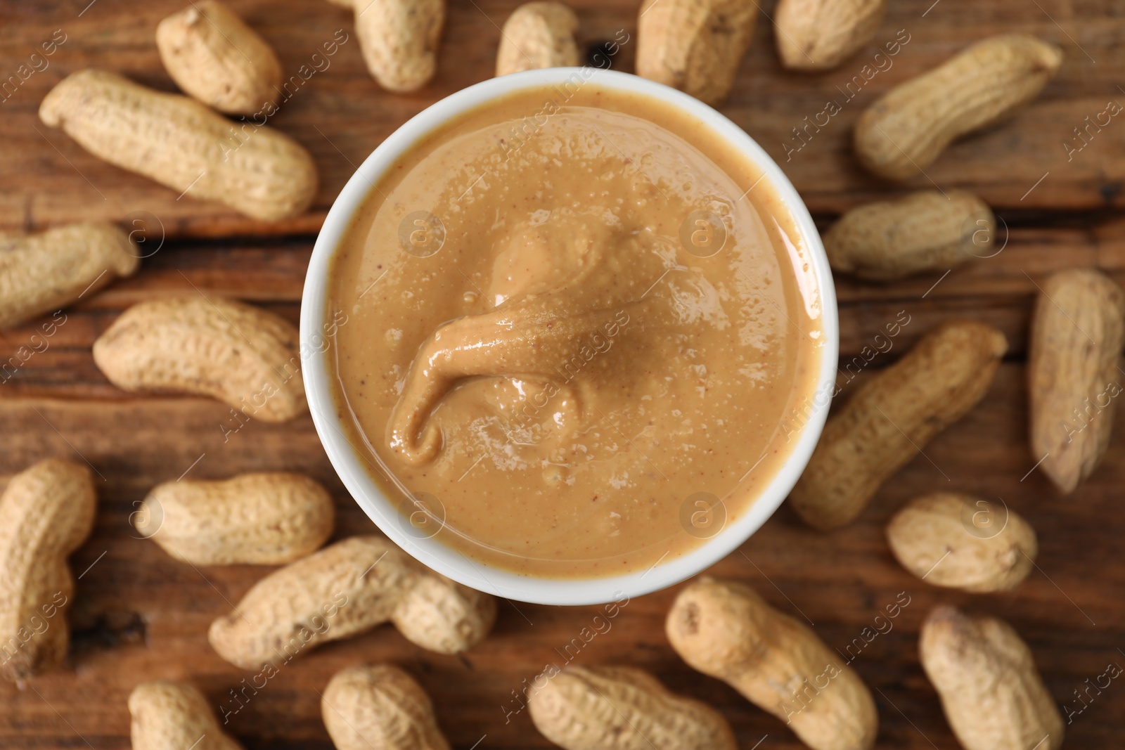 Photo of Delicious nut butter in bowl and peanuts on wooden table, top view