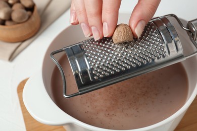 Photo of Woman grating nutmeg into cacao at table, closeup