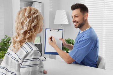 Photo of Doctor with clipboard consulting patient in clinic