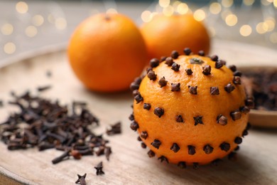 Photo of Pomander ball made of tangerine with cloves on wooden table against blurred festive lights, closeup